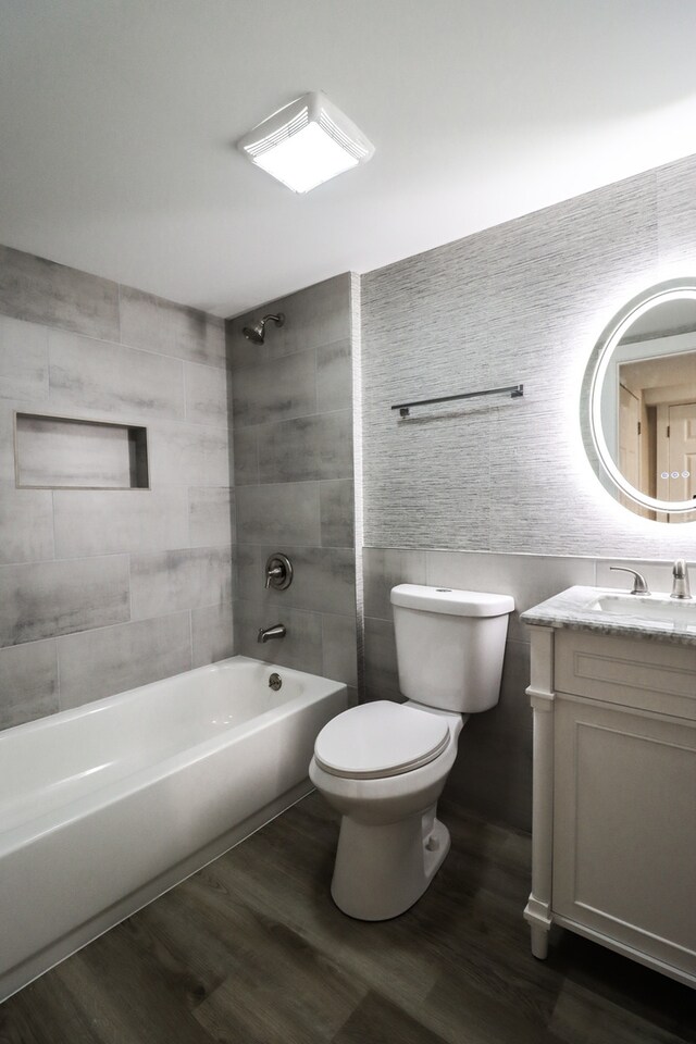 full bathroom with shower / tub combination, tile walls, hardwood / wood-style floors, vanity, and toilet