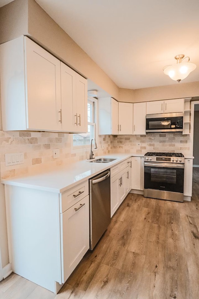 kitchen with sink, light wood-type flooring, appliances with stainless steel finishes, decorative backsplash, and white cabinets