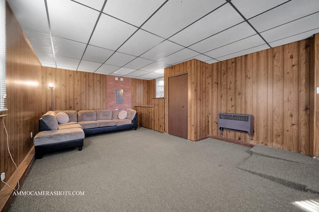 unfurnished living room featuring a paneled ceiling, wooden walls, and heating unit