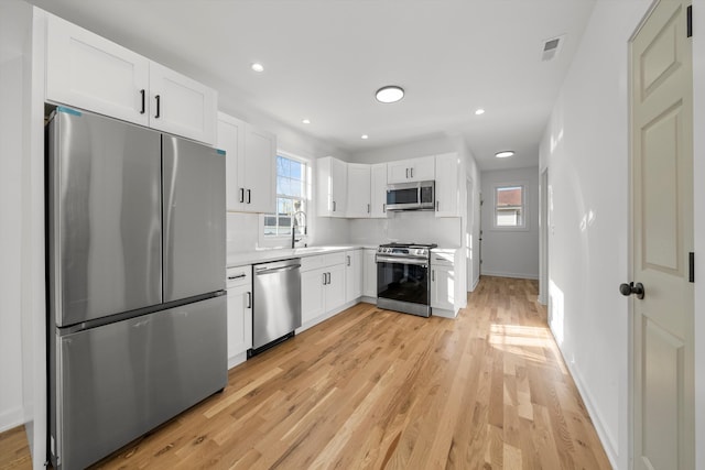 kitchen with sink, decorative backsplash, light wood-type flooring, white cabinetry, and stainless steel appliances