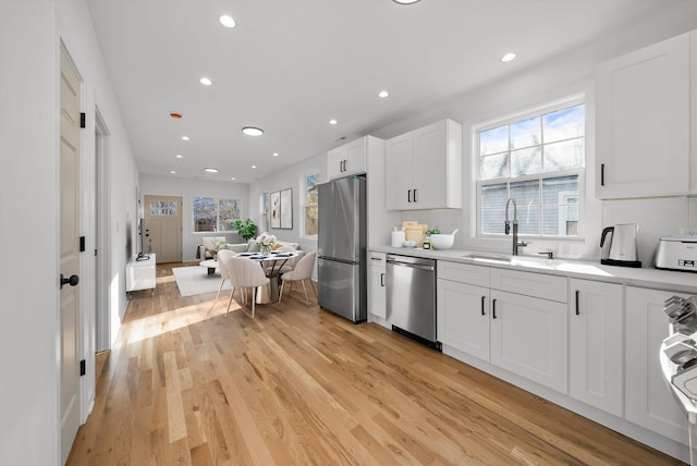 kitchen featuring sink, tasteful backsplash, light hardwood / wood-style flooring, white cabinets, and appliances with stainless steel finishes