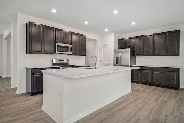 kitchen with dark brown cabinetry, sink, stainless steel appliances, light hardwood / wood-style flooring, and an island with sink