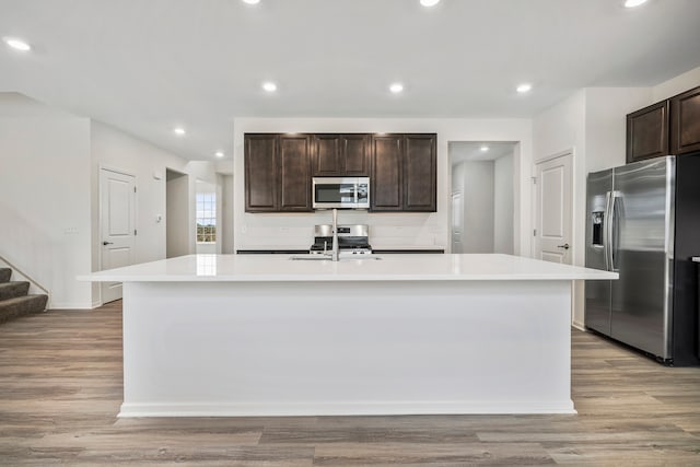 kitchen with dark brown cabinetry, a kitchen island with sink, stainless steel appliances, and light wood-type flooring