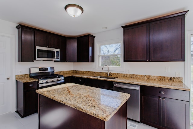 kitchen with light stone countertops, sink, a center island, dark brown cabinets, and appliances with stainless steel finishes