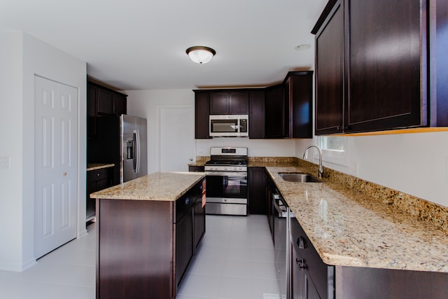 kitchen with sink, light stone countertops, dark brown cabinets, a kitchen island, and stainless steel appliances