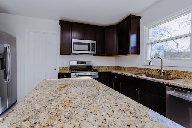 kitchen featuring dark brown cabinets, sink, light stone countertops, and stainless steel appliances