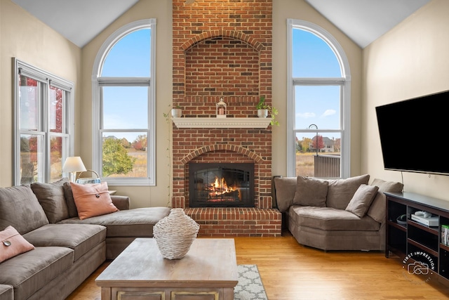 living room with light wood-type flooring, a brick fireplace, and lofted ceiling