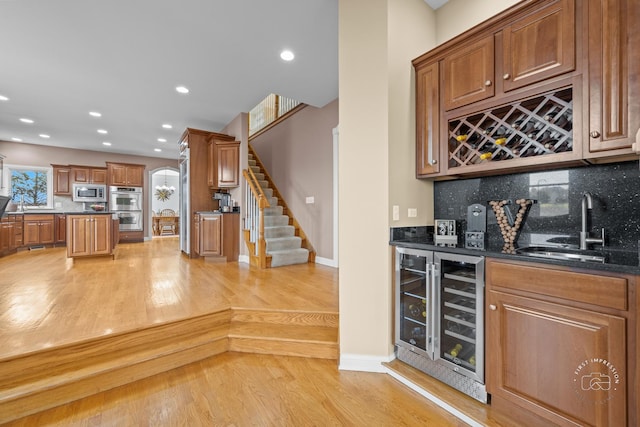 bar featuring wine cooler, light hardwood / wood-style flooring, backsplash, dark stone counters, and appliances with stainless steel finishes