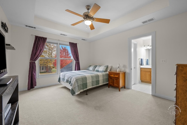 carpeted bedroom featuring a tray ceiling, ceiling fan, and ensuite bathroom