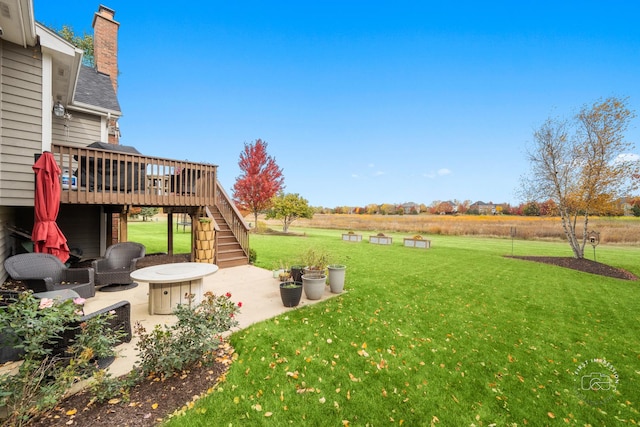 view of yard featuring a rural view, a deck, an outdoor fire pit, and a patio area