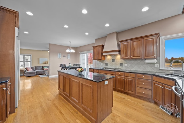 kitchen with custom range hood, sink, pendant lighting, a center island, and light hardwood / wood-style floors