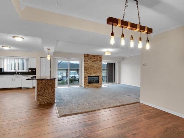 unfurnished living room featuring crown molding, sink, a stone fireplace, and hardwood / wood-style floors