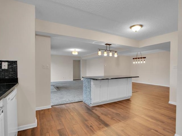 kitchen featuring tasteful backsplash, white cabinetry, hanging light fixtures, white dishwasher, and light hardwood / wood-style flooring