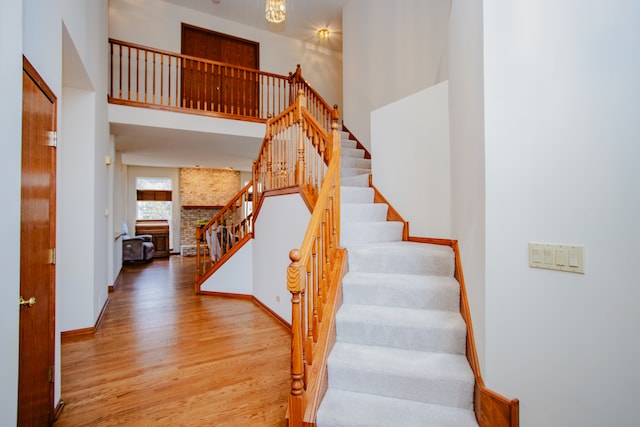 staircase with a fireplace, wood-type flooring, a high ceiling, and brick wall