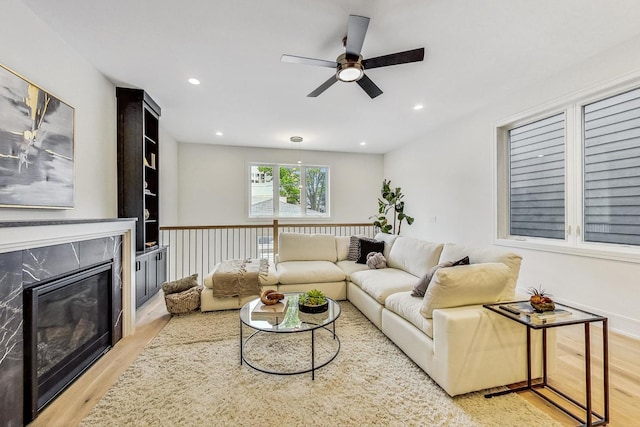 living room featuring a high end fireplace, light hardwood / wood-style flooring, and ceiling fan