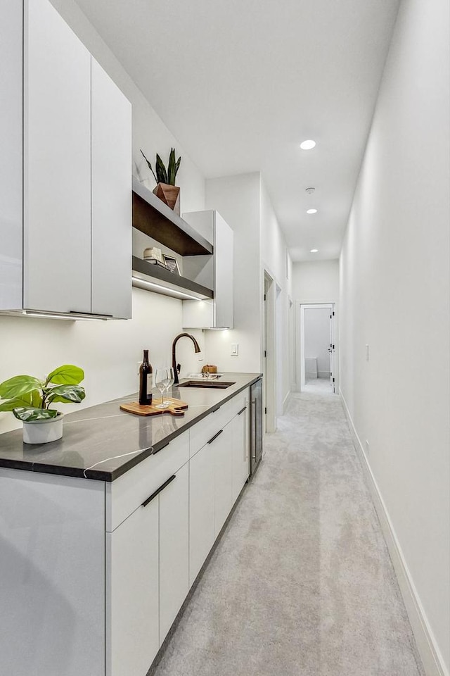 kitchen with light carpet, white cabinetry, dark stone countertops, and sink