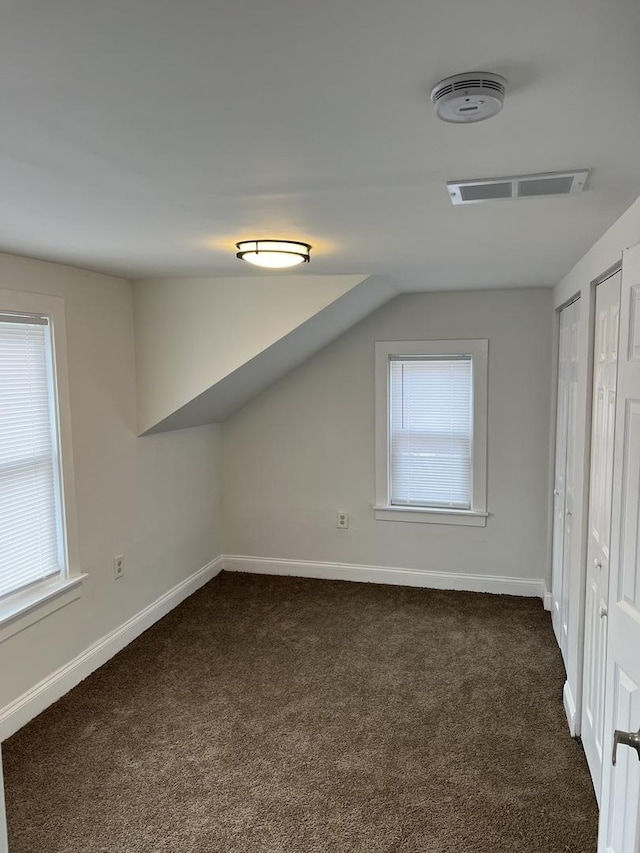 additional living space featuring plenty of natural light, dark carpet, and vaulted ceiling