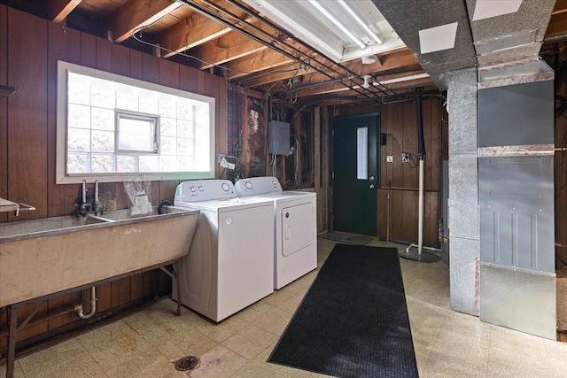 clothes washing area featuring washing machine and dryer, wooden walls, and sink