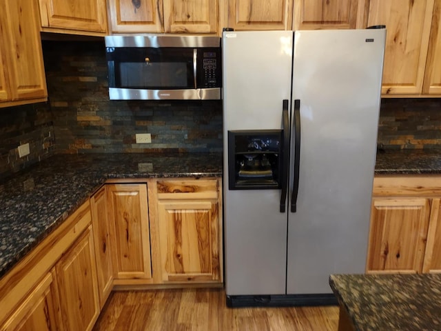 kitchen with stainless steel appliances, light hardwood / wood-style floors, and dark stone counters