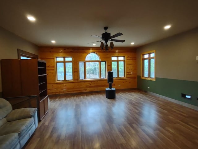 unfurnished living room featuring ceiling fan, dark hardwood / wood-style flooring, and wood walls