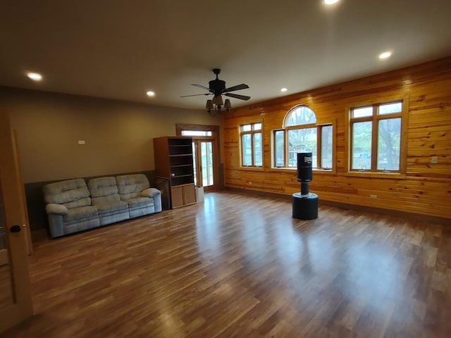 unfurnished living room featuring ceiling fan, dark hardwood / wood-style flooring, and wooden walls