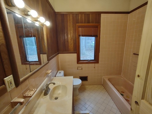 bathroom featuring toilet, a tub to relax in, tile walls, tile patterned floors, and sink