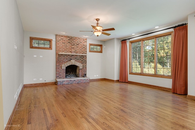 unfurnished living room featuring ceiling fan, a brick fireplace, and light wood-type flooring