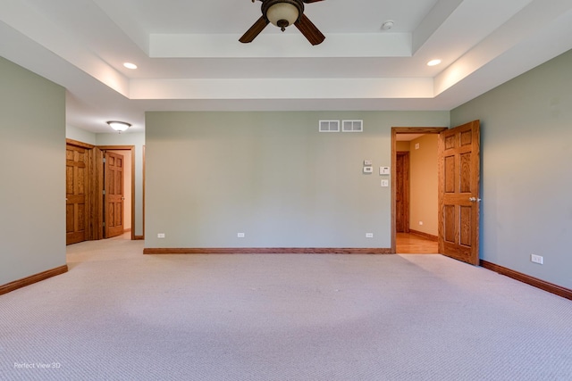 empty room with a raised ceiling, light colored carpet, and ceiling fan