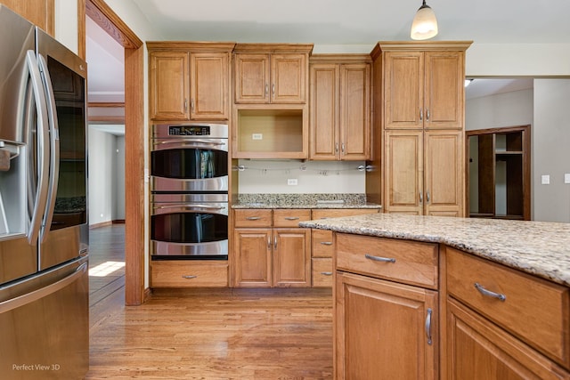 kitchen with light stone counters, appliances with stainless steel finishes, hanging light fixtures, and light wood-type flooring