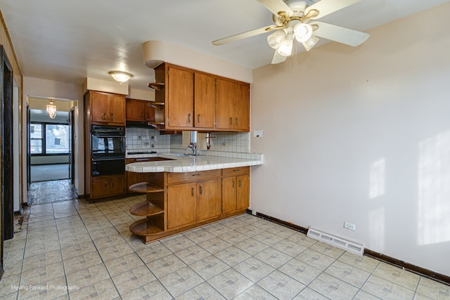 kitchen featuring ceiling fan, tasteful backsplash, kitchen peninsula, tile countertops, and black oven