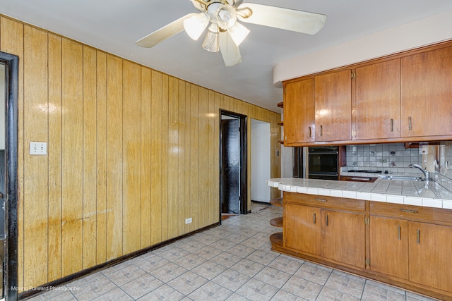 kitchen featuring decorative backsplash, ceiling fan, sink, tile countertops, and black oven