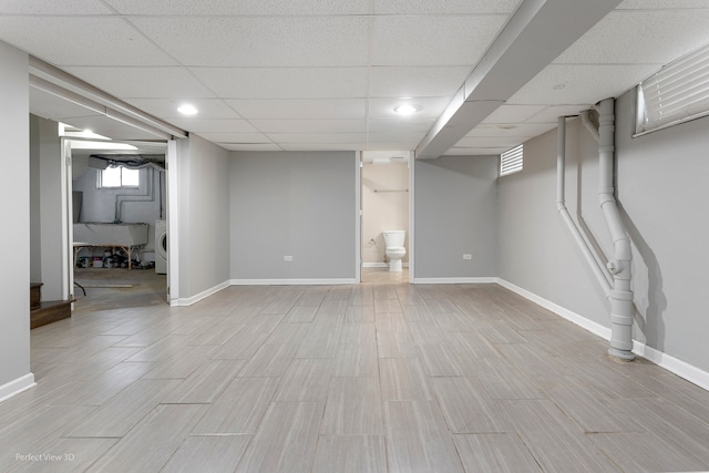 basement featuring a paneled ceiling, washer / dryer, and light wood-type flooring