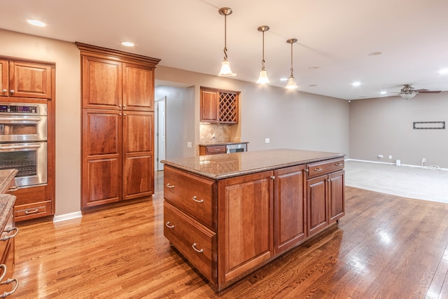 kitchen with a center island, dark stone counters, hardwood / wood-style flooring, ceiling fan, and double oven