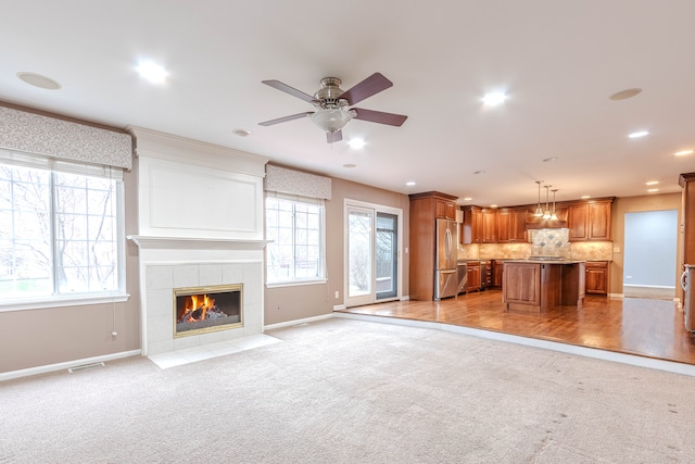 unfurnished living room featuring ceiling fan, a tiled fireplace, and light hardwood / wood-style flooring