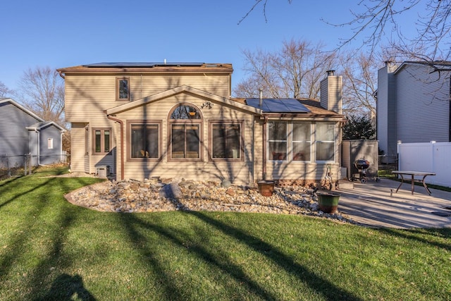 rear view of property featuring solar panels, a patio, a sunroom, and a lawn