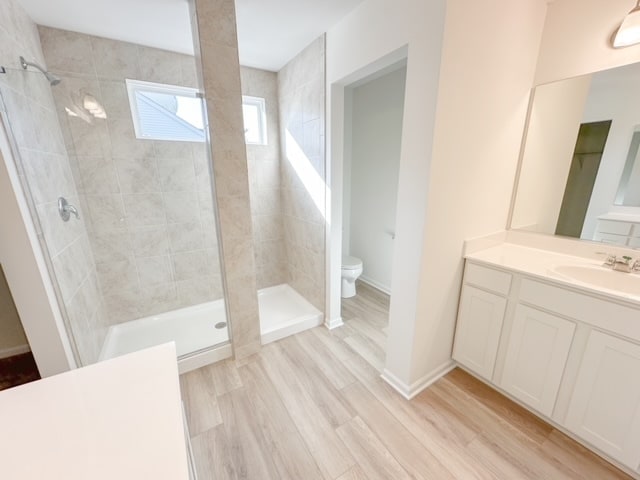 bathroom with vanity, toilet, wood-type flooring, and a tile shower