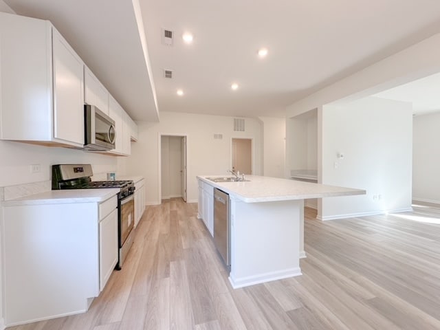 kitchen featuring stainless steel appliances, sink, light hardwood / wood-style flooring, white cabinets, and an island with sink