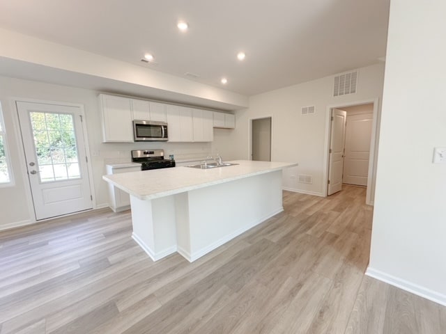 kitchen with sink, light hardwood / wood-style flooring, an island with sink, white cabinets, and appliances with stainless steel finishes