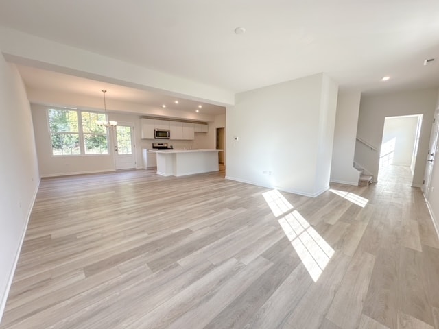 unfurnished living room with light wood-type flooring and a chandelier