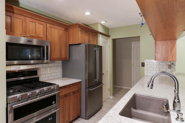 kitchen with light stone countertops, sink, decorative backsplash, light tile patterned flooring, and appliances with stainless steel finishes