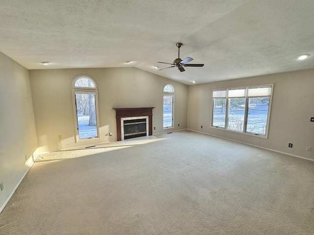 unfurnished living room with ceiling fan, a premium fireplace, a textured ceiling, vaulted ceiling, and light carpet