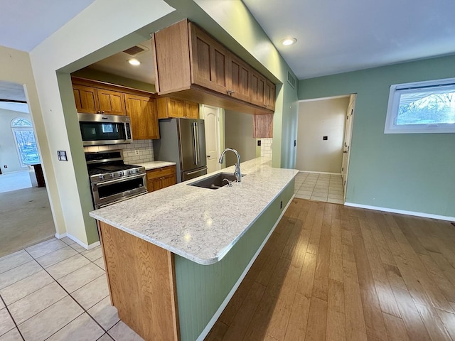 kitchen with light stone countertops, sink, backsplash, kitchen peninsula, and appliances with stainless steel finishes