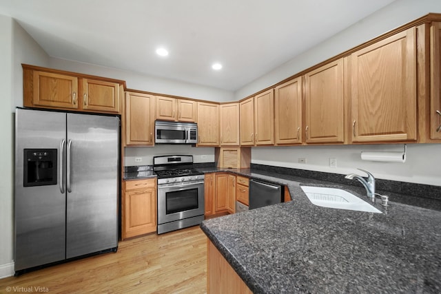 kitchen with light hardwood / wood-style floors, sink, stainless steel appliances, and dark stone counters