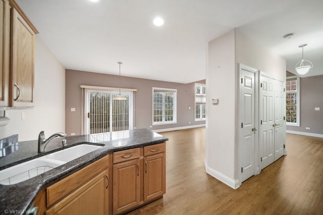 kitchen with hardwood / wood-style flooring, decorative light fixtures, sink, and dark stone counters