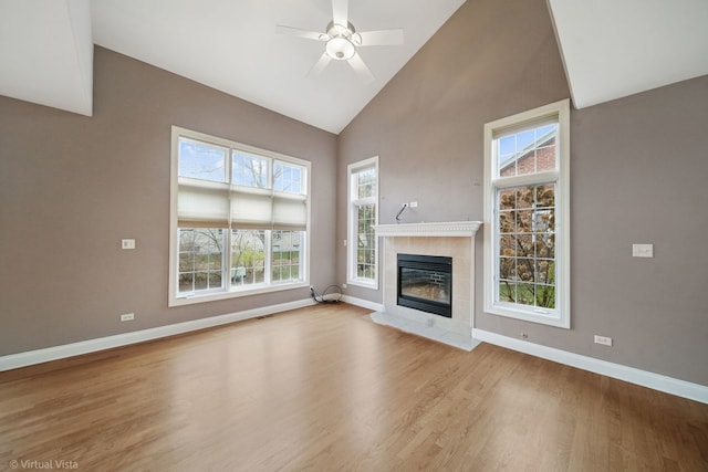 unfurnished living room with a tiled fireplace, ceiling fan, high vaulted ceiling, and light hardwood / wood-style floors