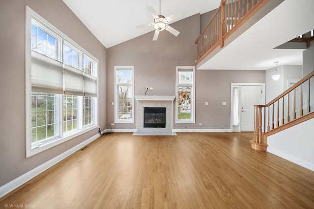 unfurnished living room with wood-type flooring, high vaulted ceiling, ceiling fan, and a tiled fireplace