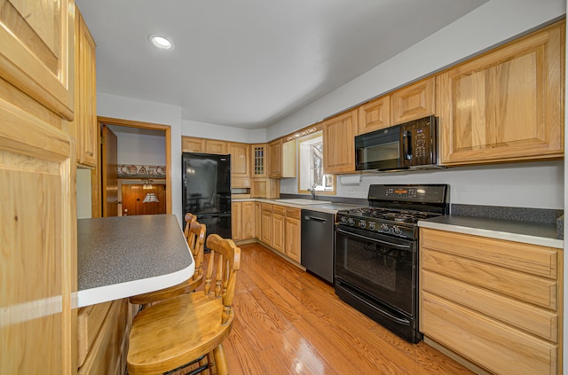 kitchen with sink, light brown cabinetry, black appliances, and light hardwood / wood-style floors