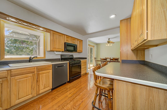 kitchen with ceiling fan, sink, a kitchen bar, black appliances, and light wood-type flooring