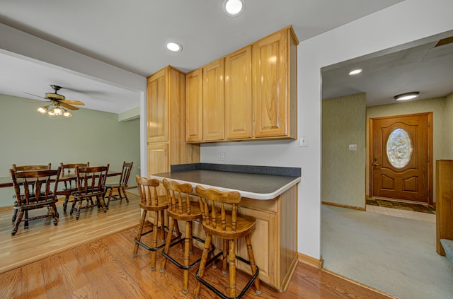 kitchen with light brown cabinetry, light hardwood / wood-style flooring, ceiling fan, and a breakfast bar area