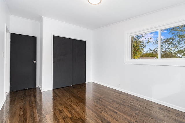 unfurnished bedroom with ornamental molding, dark wood-type flooring, and a closet